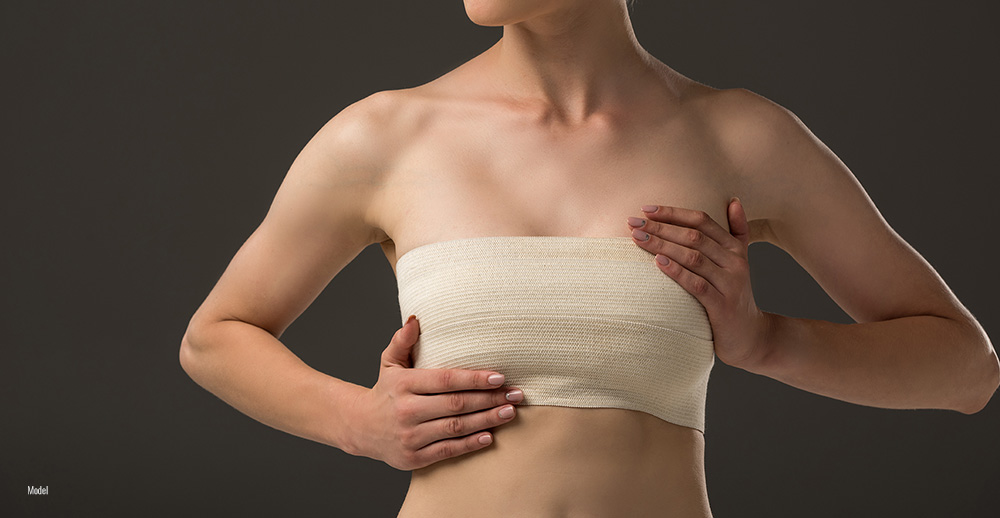 A woman holds her wrapped breasts after cosmetic breast surgery.