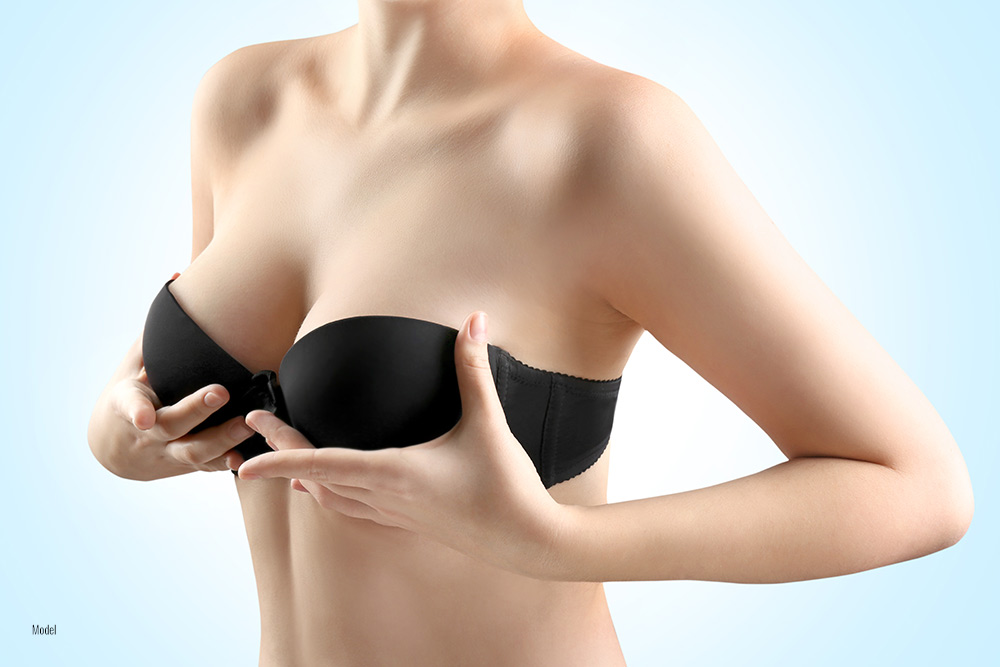 A woman in a black bra lifts her breasts with her hands